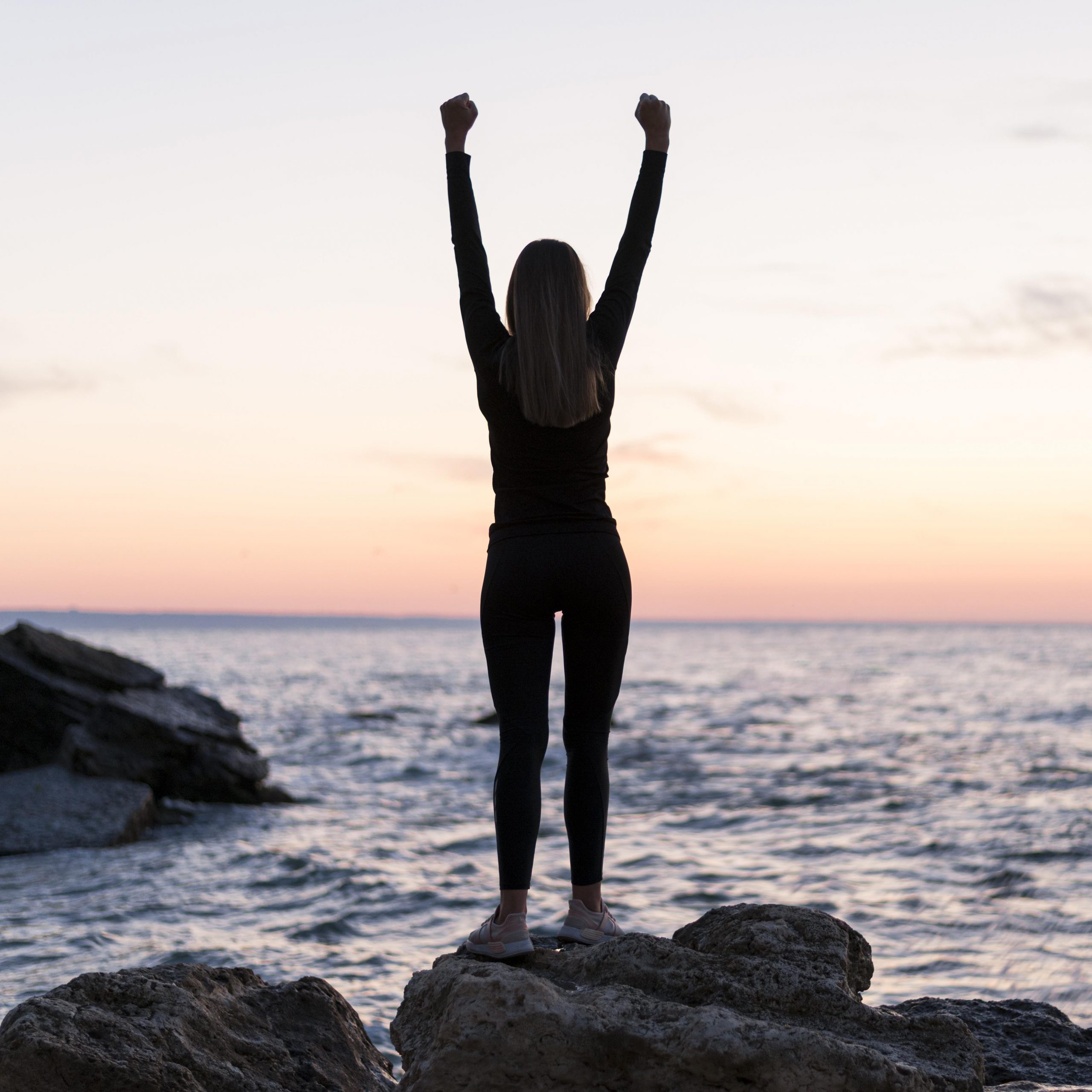 femme-debout-sur-une-cote-avec-ses-bras-vers-le-haut